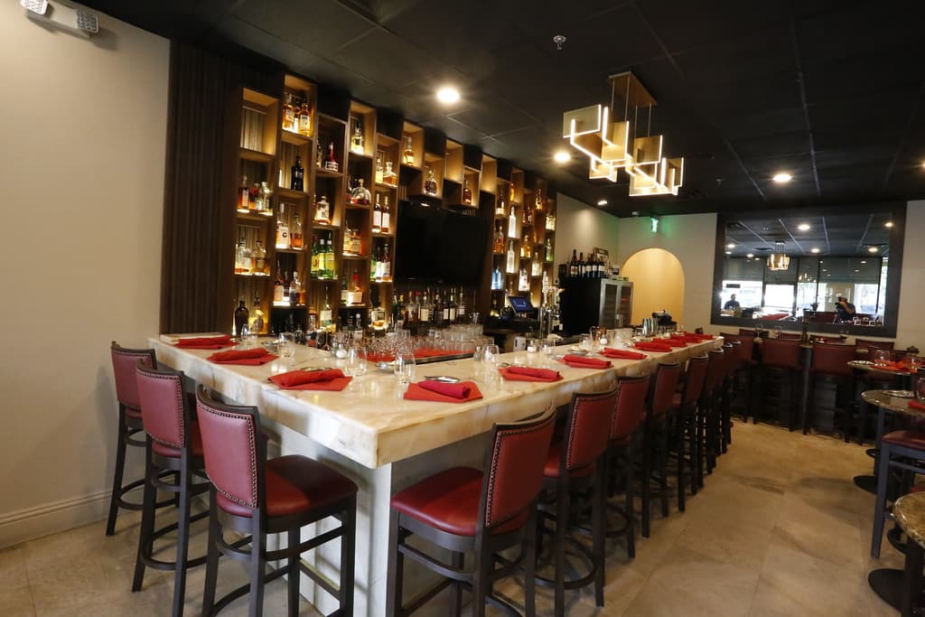Modern restaurant bar at Cibao Grille featuring marble countertops, red leather bar stools, premium liquor display, and an upscale fine dining atmosphere.